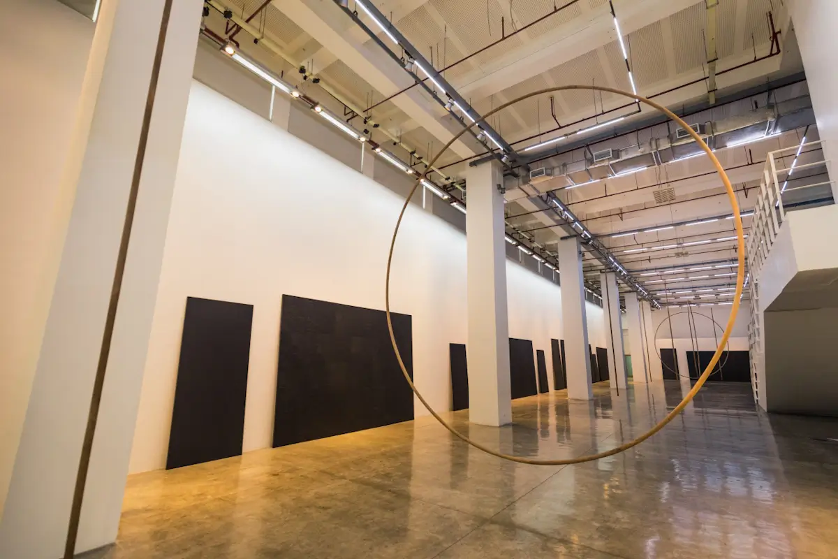 A modern art gallery, one of the standout Manila tourist spots, features large black rectangular artworks on white walls and a thin circular metal sculpture suspended from the ceiling. Polished concrete floors gleam under bright overhead lights.