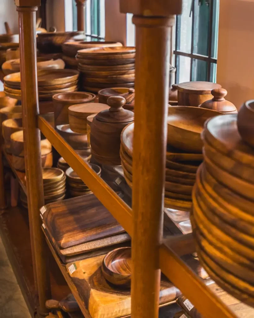Shelves filled with stacks of round and rectangular wooden plates, bowls, and trays of various sizes are displayed in a well-lit shop next to windows—a charming find among Manila tourist spots.