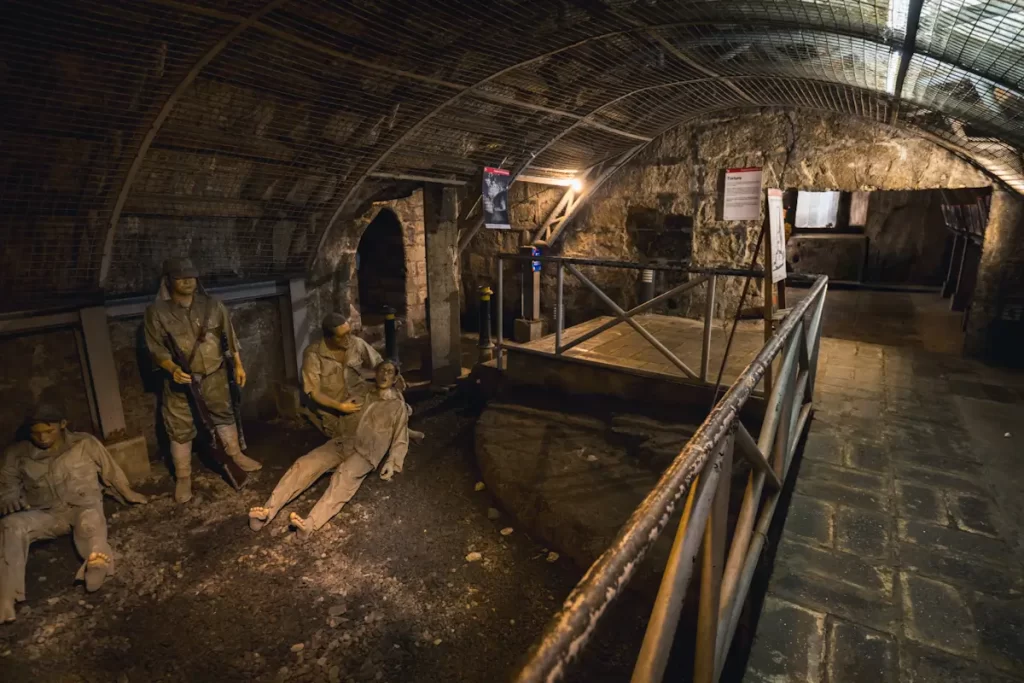 A dimly lit underground tunnel, one of the unique Manila tourist spots, features life-sized statues of miners in work clothes—some sitting, some standing—against stone walls, with metal railings and informational signs lining the walkway.