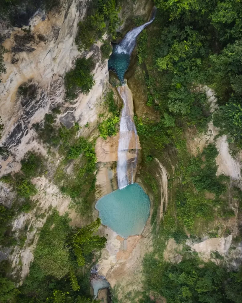 Aerial view of Dao Falls, a multi-tiered waterfall cascading down rocky cliffs into turquoise pools, surrounded by dense green vegetation.