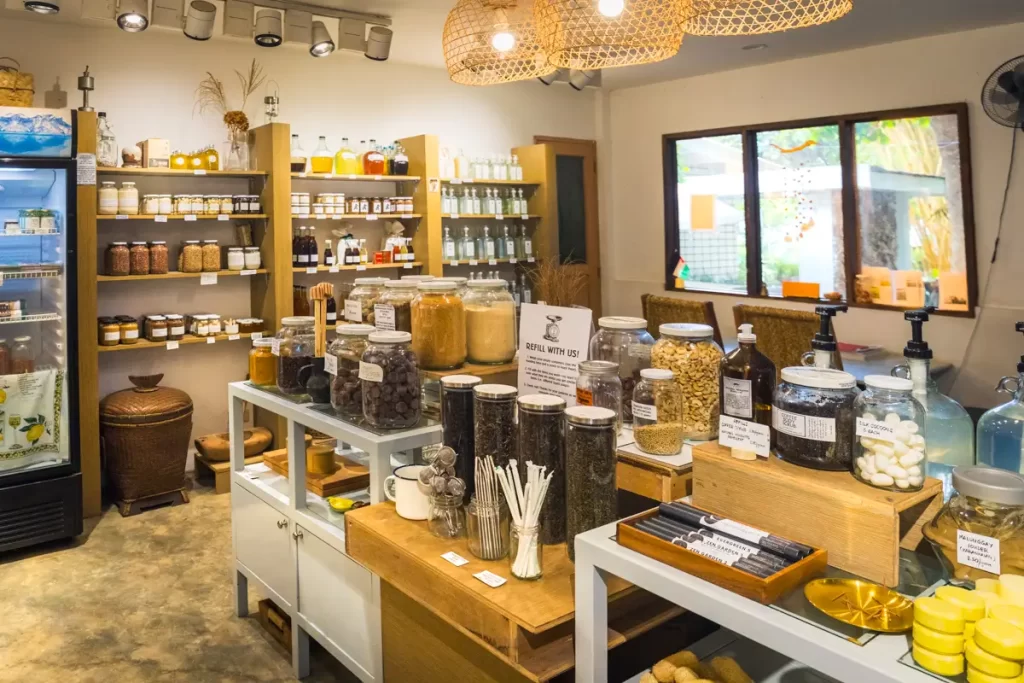 Interior of a small store in Dumaguete Tourist Spots, with shelves and tables displaying jars filled with various dry goods, glass bottles, and natural products; a refrigerator and additional jars are visible in the background.
