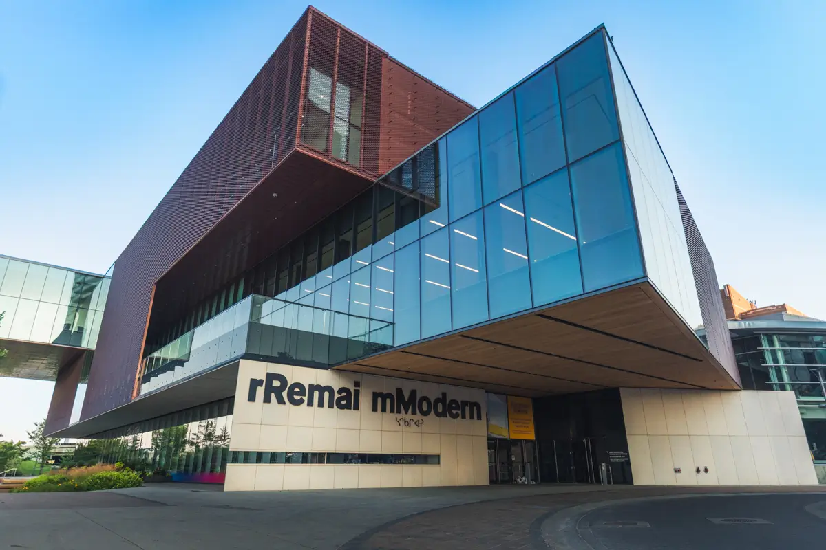 A modern building with large glass panels and angular architecture, Remai mModern stands out among Saskatoon attractions. The structure features an overhang and is connected to another section via a glass walkway.