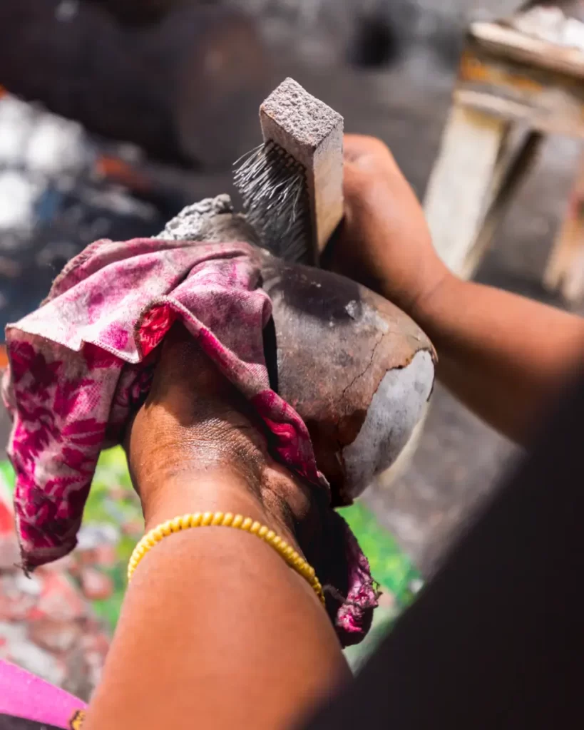A person in Bohol holds a coconut with a pink cloth and uses a wire brush to clean its surface. Wearing a yellow beaded bracelet, they work carefully, while the background remains blurred.