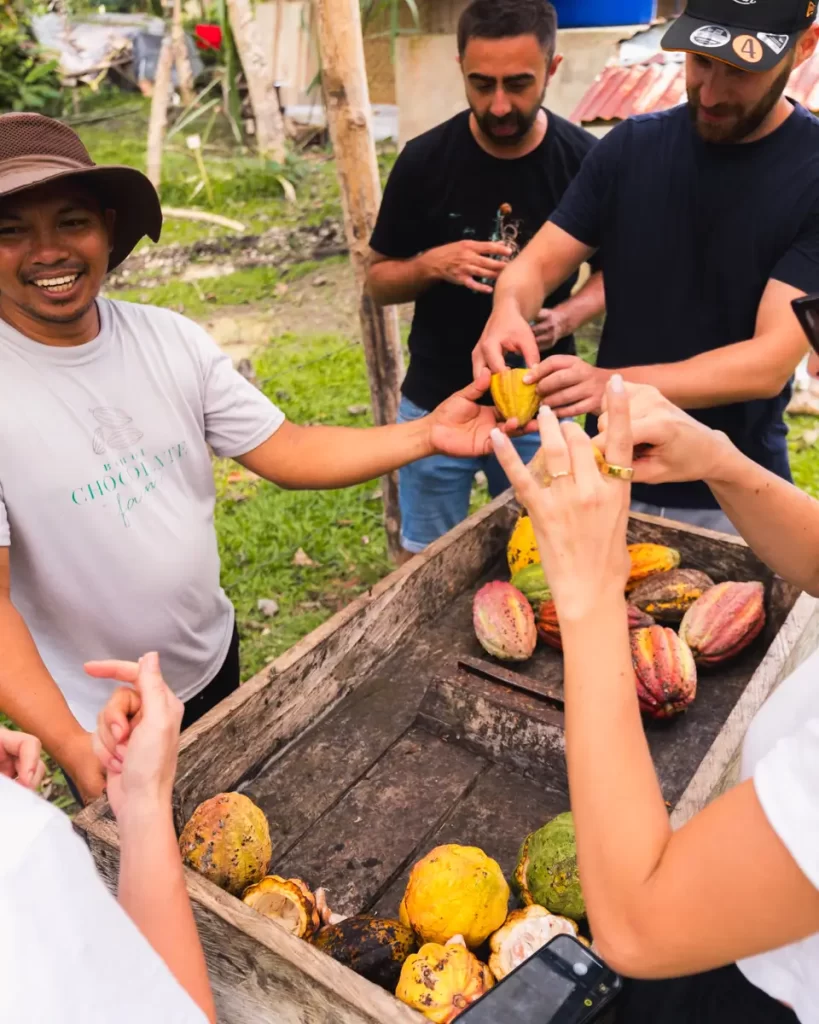 Several people stand around a wooden cart holding cacao pods in rural Bohol. Some of the pods are open, and one man is smiling as the group examines or handles them outdoors.