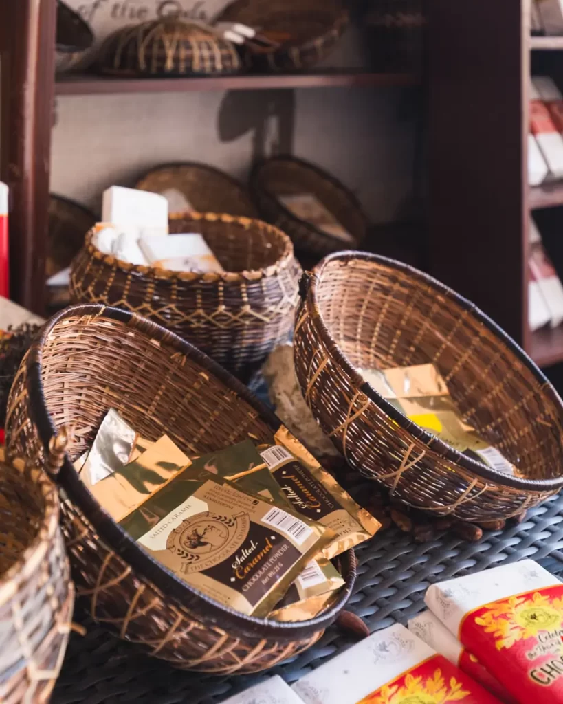 Wicker baskets on a table, some containing gold and white packaged goods inspired by Bohol. Additional baskets and packaged items are visible on shelves in the background.