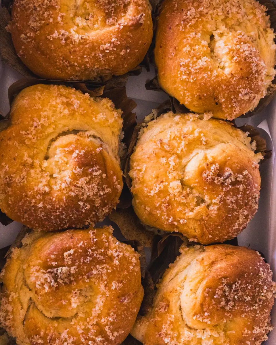 Six golden-brown, round pastries topped with a crumbly sugar topping are arranged closely together in a box. Inspired by flavors from Bohol, the pastries have a slightly swirled shape and appear freshly baked.