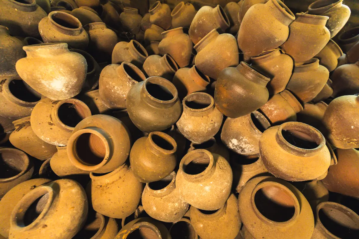 A large pile of empty, round, brown clay pots stacked haphazardly, with their wide openings facing different directions. These weathered pots, often seen in Vigan tourist spots, have patches of white residue on some surfaces.