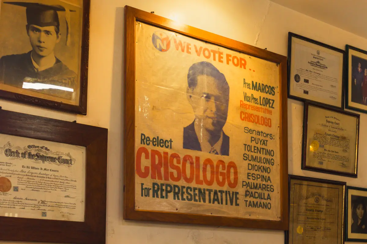 A framed vintage election poster for candidate Crisologo is displayed on a wall alongside certificates and portraits, offering a glimpse into local history. It’s one of the unique Vigan attractions often highlighted in any Vigan travel guide.