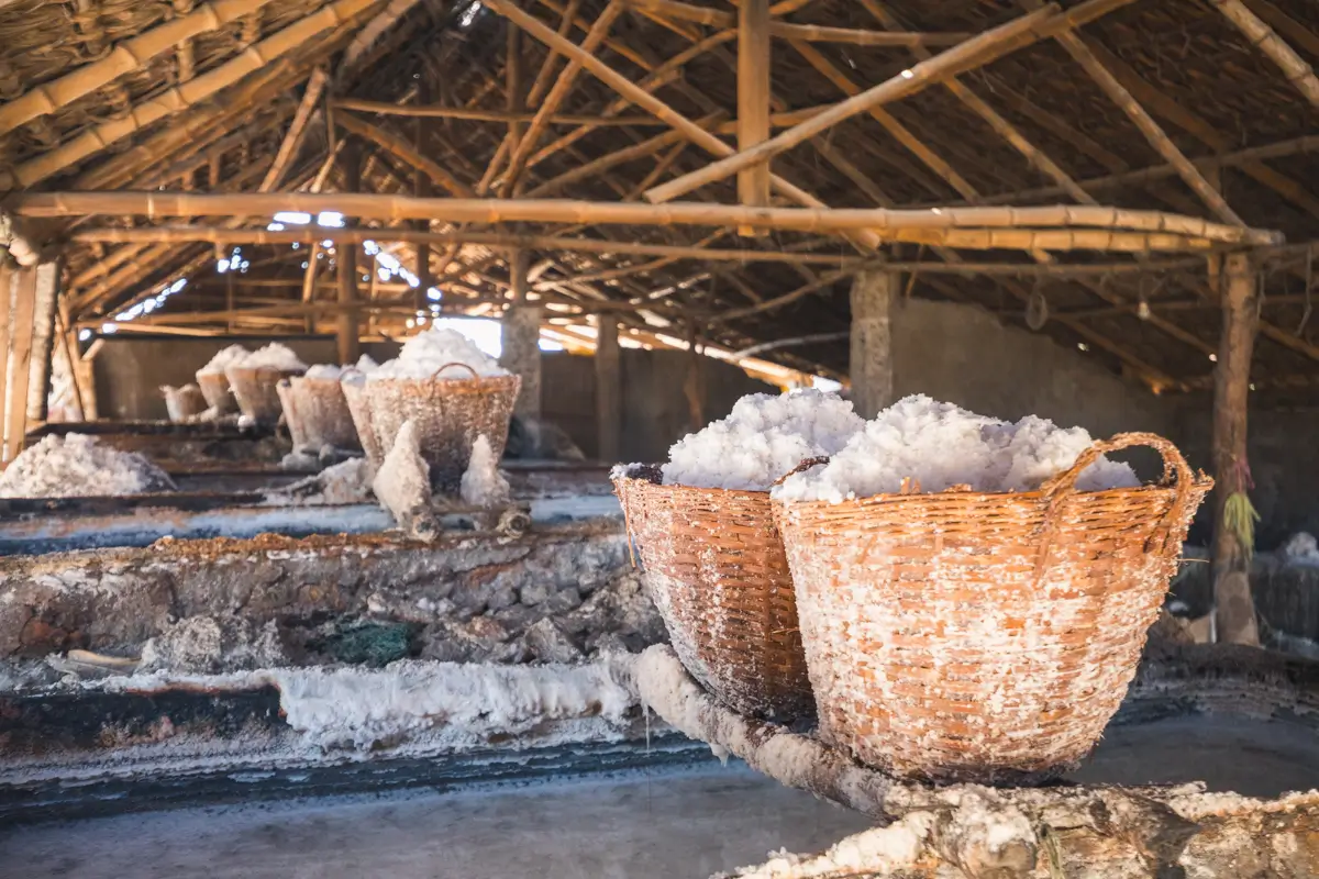 Wicker baskets filled with crystallized salt are placed inside a rustic, open-roofed structure with wooden beams—a hidden gem among the best Vigan tourist spots, where salt deposits are visible on surfaces throughout the area.