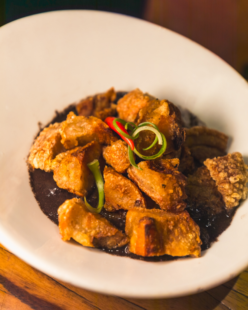A white plate filled with crispy golden-brown fried pork pieces arranged atop a dark sauce, garnished with thinly sliced green and red chili peppers—a must-try dish featured in many Vigan travel guides and popular at the best places in Vigan.