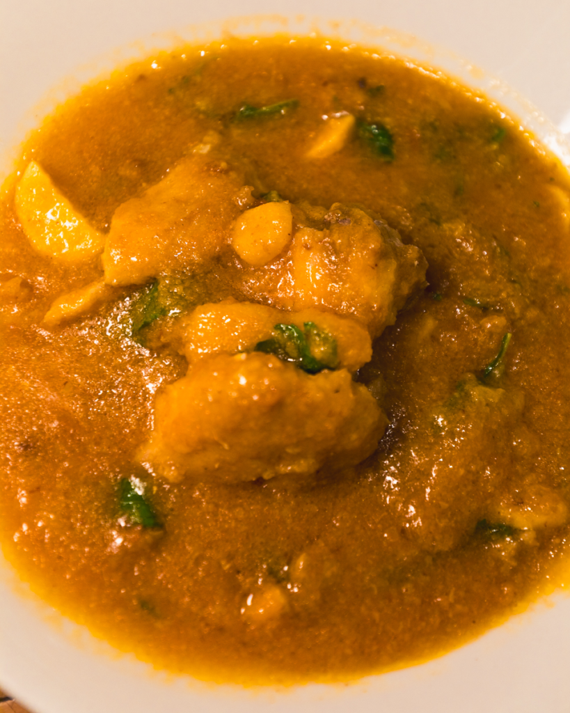 A close-up of a bowl filled with thick, orange-brown curry with chunks of meat or vegetables and visible herbs, served in a white dish—a must-try for food lovers exploring Vigan tourist spots.
