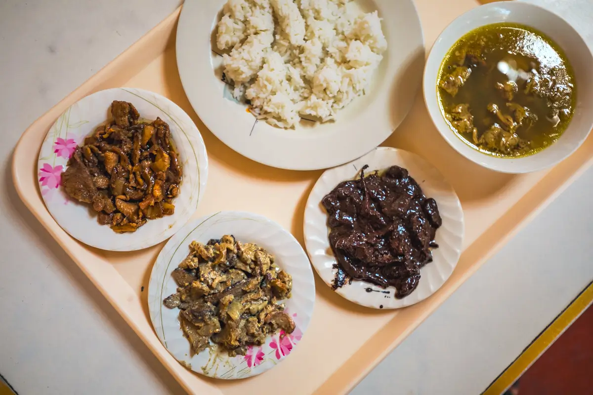 A beige tray holds four plates and a bowl: one plate of white rice, three plates of cooked meats, and a bowl of soup with meat in a yellowish broth—like the flavors you’ll find at the best places in Vigan, according to any Vigan travel guide.