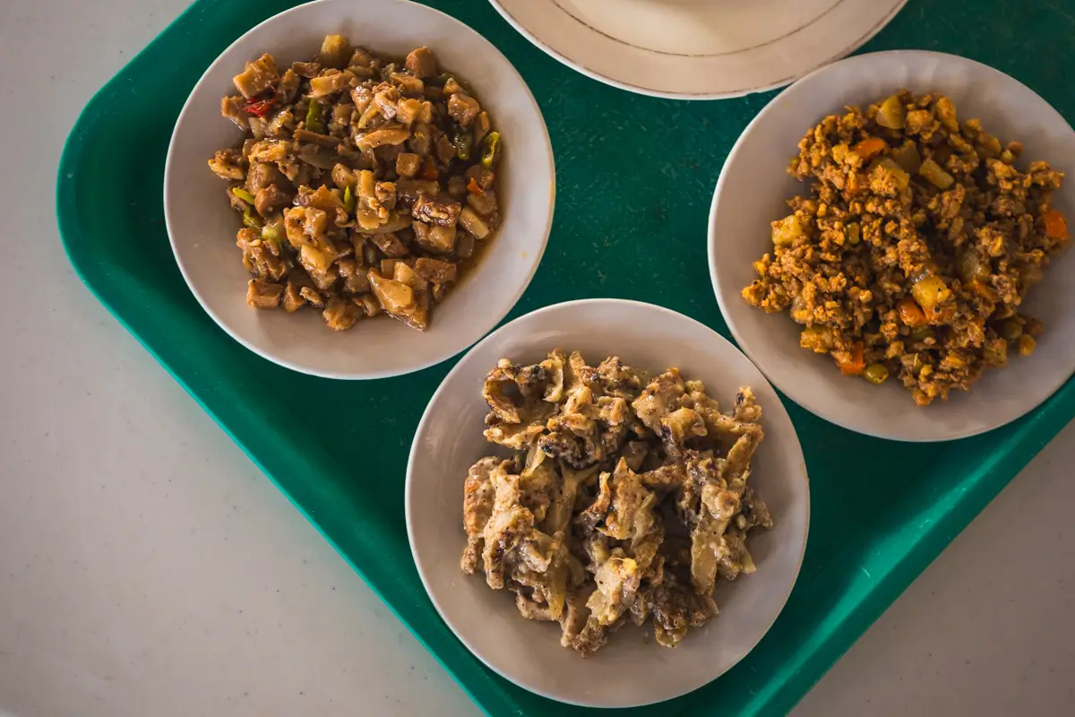 Three white bowls with different cooked dishes are placed on a green tray—a vibrant glimpse into local flavors that should not be missed in any Vigan travel guide, especially when exploring the best places in Vigan.
