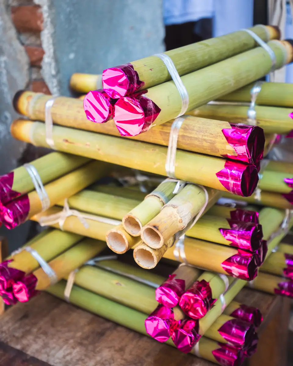 Several bundles of green bamboo tubes are stacked together, each tube sealed at one end with shiny pink foil. These unique items, tied with white string and set against a rustic backdrop, showcase the local charm found in Vigan tourist spots.