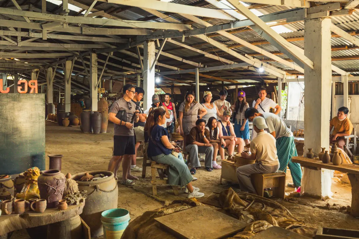 A group of people watch a pottery-making demonstration inside a rustic, open-sided workshop with wooden beams and pottery pieces—a must-see highlight often featured in any Vigan Travel Guide exploring the best places in Vigan.