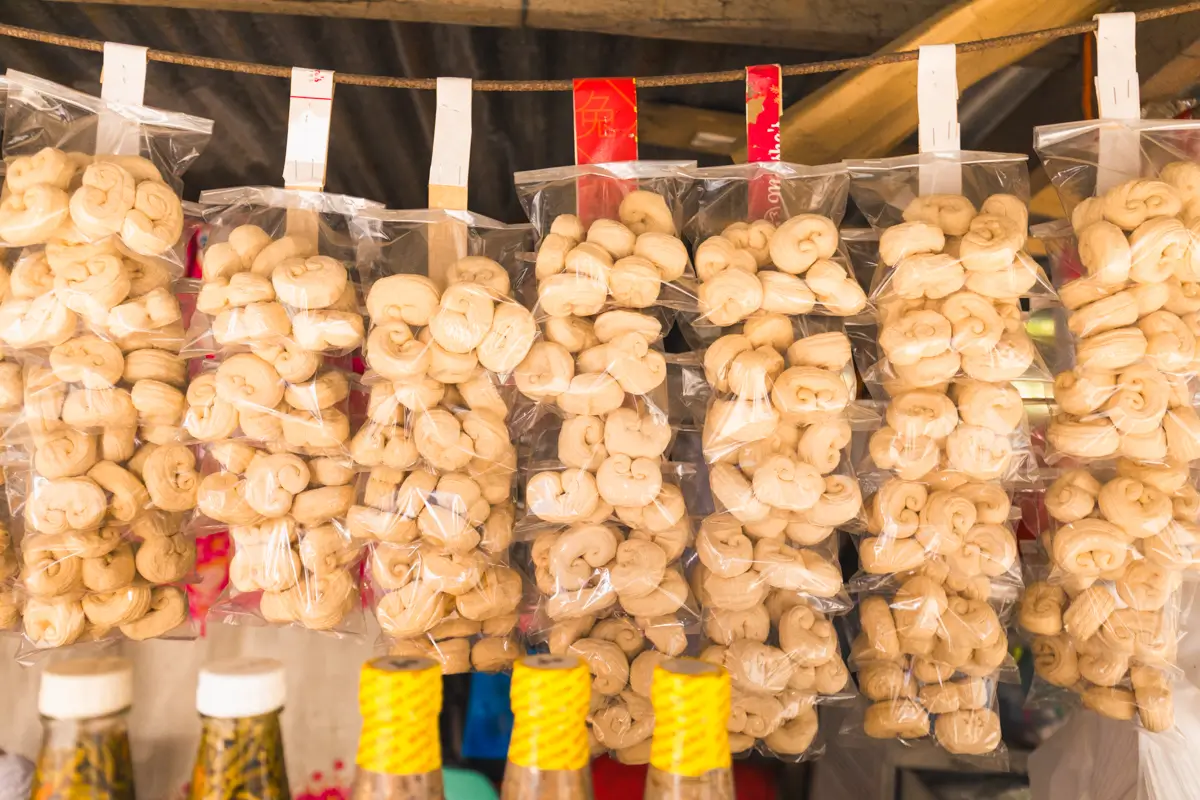 Several clear plastic bags filled with round, light-colored snacks hang on a clothesline with clothespins; bottles with yellow-tied lids sit below. Discover these local treats as you explore the best places in Vigan using a handy Vigan travel guide.