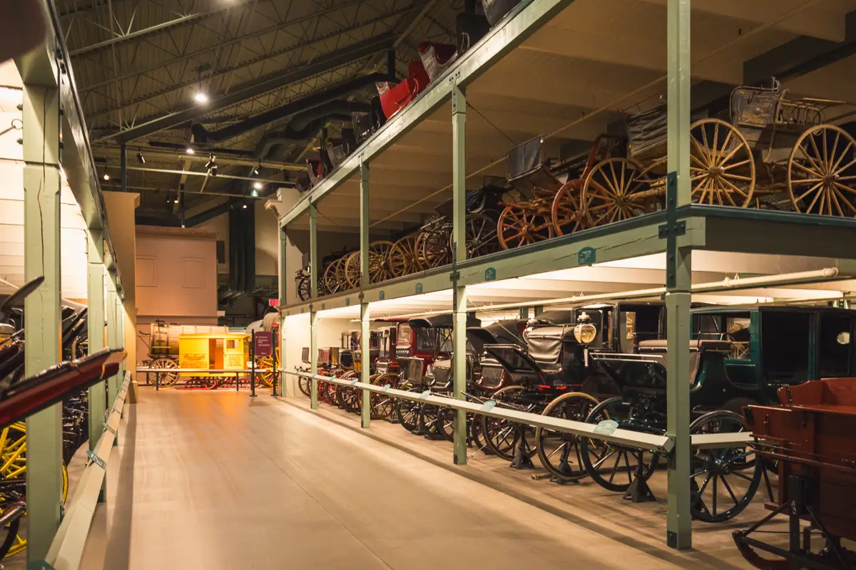 Rows of vintage carriages and wagons are displayed on two levels in a well-lit Lethbridge museum exhibit, featuring a high ceiling and spacious walkway.