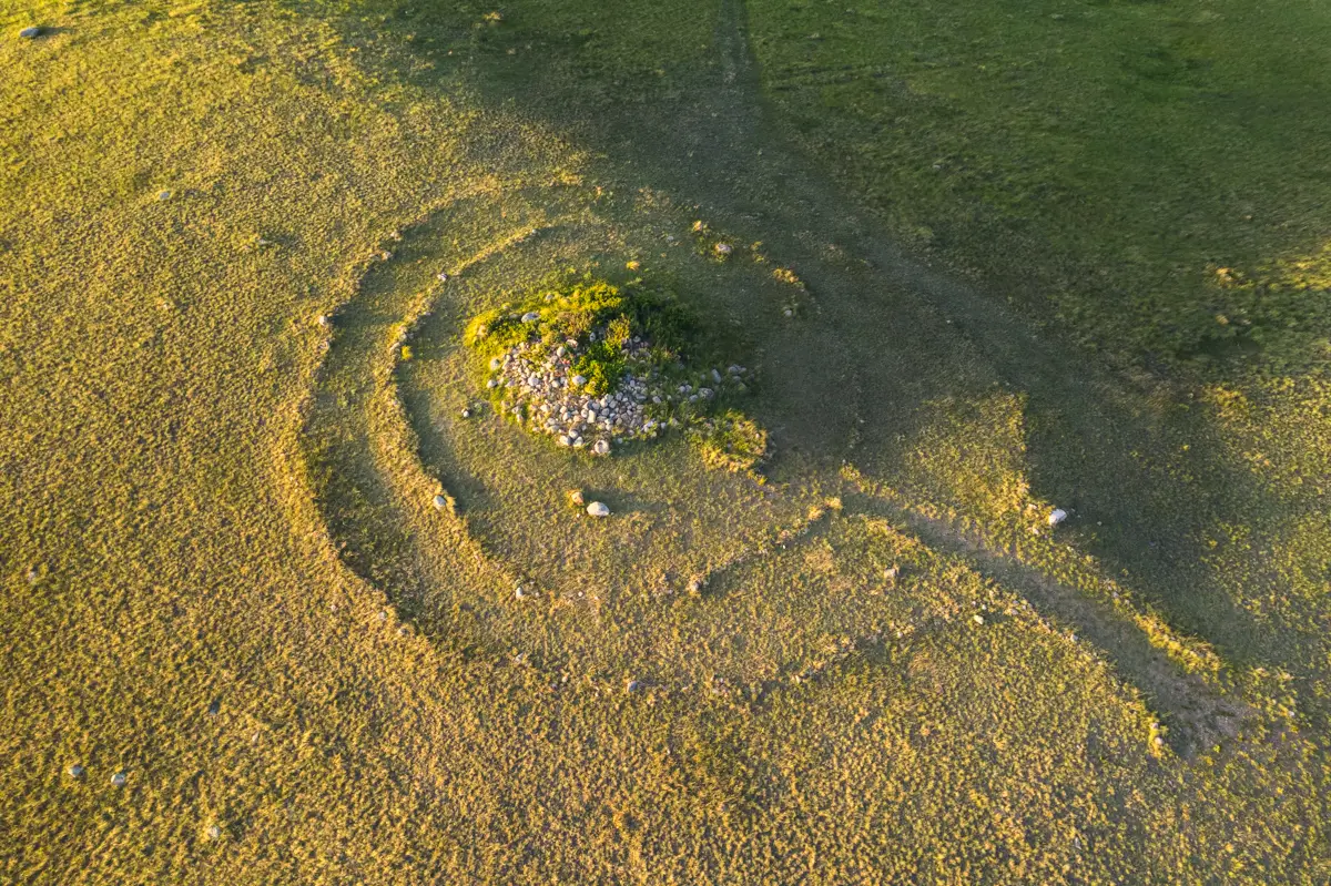 Aerial view of a grassy field near Lethbridge, featuring circular stone formations and a mound of rocks at the center, surrounded by patches of green grass and earth.