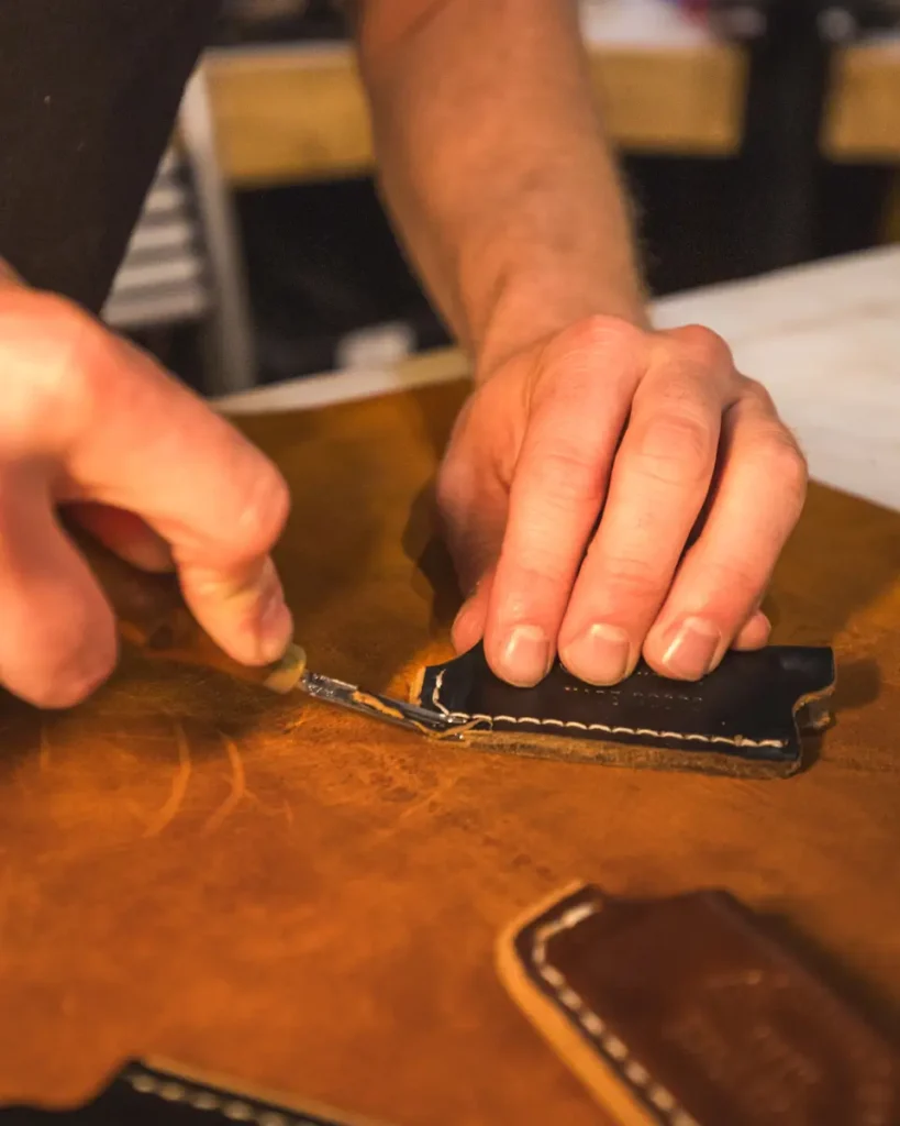 A person in Lethbridge uses a small knife to carefully trim excess leather from the edge of a stitched leather piece on a workbench.