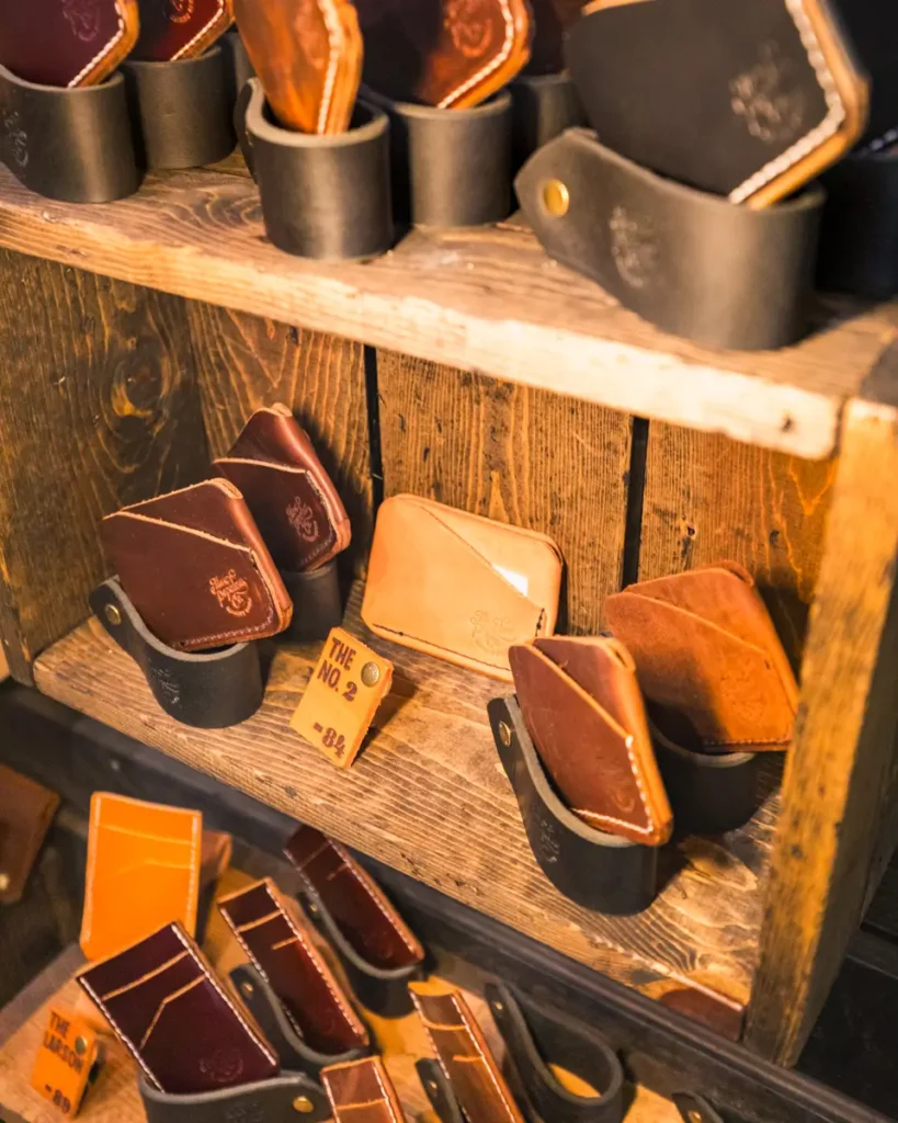 Leather wallets and cardholders in brown and tan shades are displayed on wooden shelves, each placed inside black holders. The shelves, crafted with a rustic, wooden texture reminiscent of classic Lethbridge style, feature a small tag labeled The No. 2 that is visible among the elegant accessories.