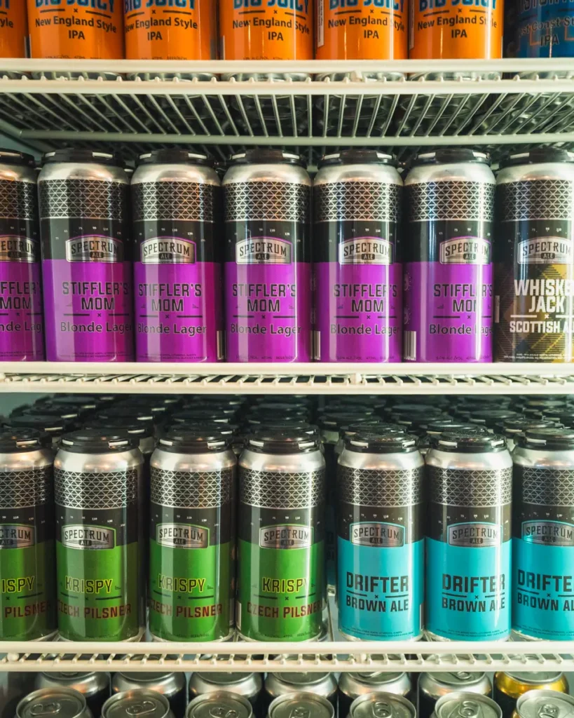 Cans of Spectrum beer, including Stifflers Mom Blonde Lager, Krispy Czech Pilsner, and Drifter Brown Ale, are lined up on shelves in a refrigerator at a Lethbridge store.